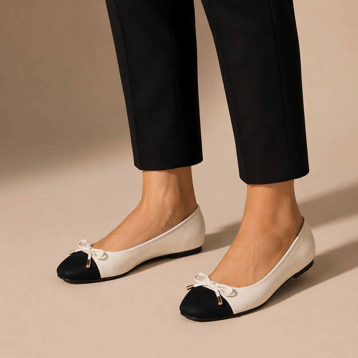 Crèmekleurige ballerina's met zwarte neus en strik, gedragen onder een zwarte enkelbroek.