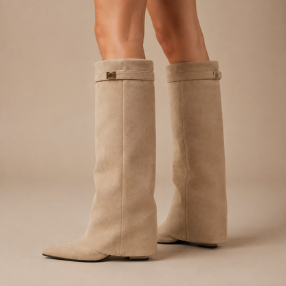 Beige kniehoge dameslaarzen met puntneus en sierband, schuin van voren gedragen.