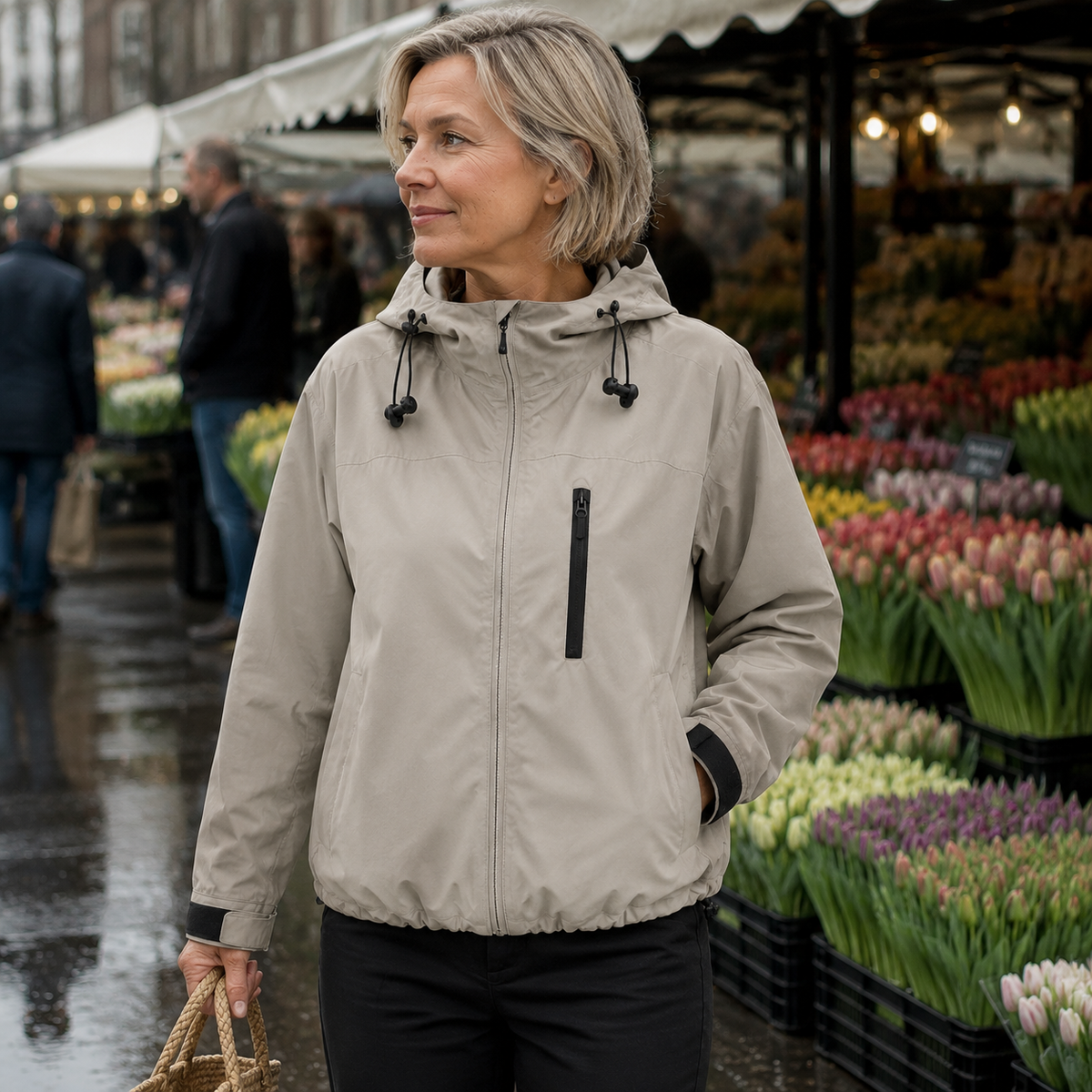 Beige korte damesjas met capuchon en ritszak, gedragen op een bloemenmarkt.