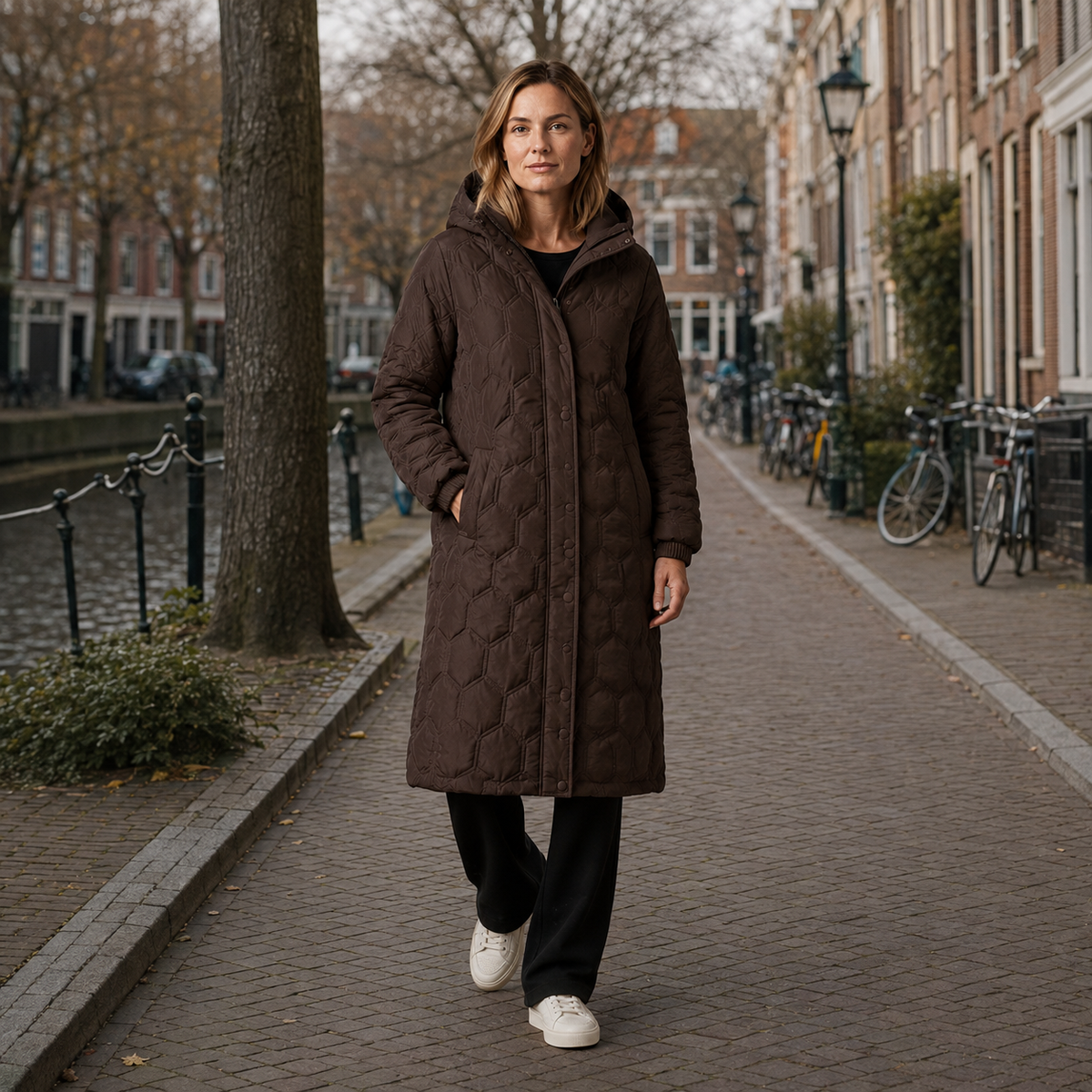 Bruine lange gewatteerde dameswinterjas, gedragen tijdens een wandeling langs een gracht.