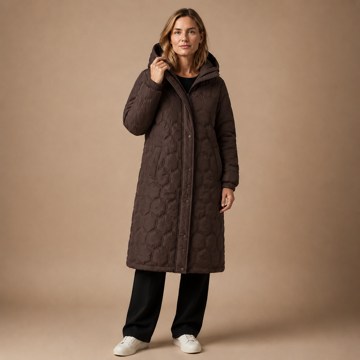 Bruine lange damesjas met capuchon en zakken, gedragen met een zwarte wijde broek.