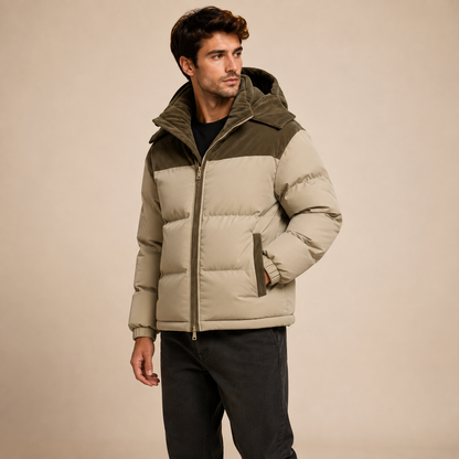 Beige gewatteerde herenwinterjas met bruine capuchon en schouderdetails, schuin van voren.
